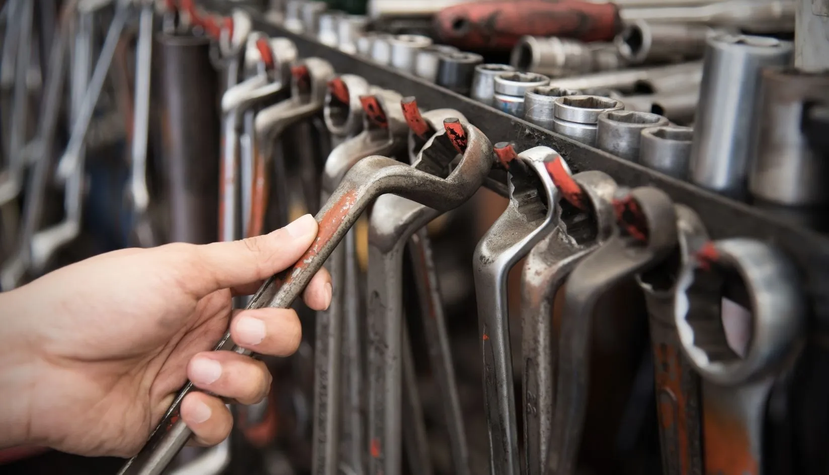 Close‑up of a worker’s hand selecting a marked combination wrench from an organized workshop tool rack.